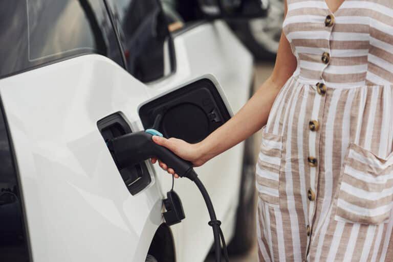 Woman on the electric cars charge station at daytime. Brand new vehicle