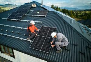 Technicians installing photovoltaic solar panels on roof of house.